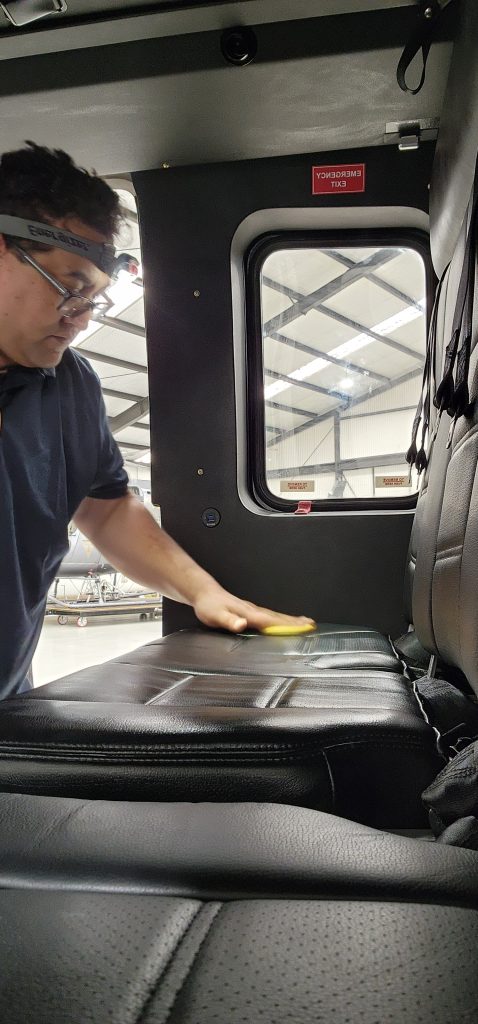Skyshine Ltd technician polishing black leather aircraft seating inside a hangar, focusing on detail and finish quality.